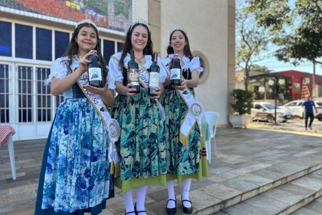 A 14ª edição da Festa do Vinho de Santana, tradicional evento da colônia tirolesa de Piracicaba, acontece neste feriado prolongado, de 20 a 22 de junho, na praça Bortolo Vitti, com programação que inclui apresentações artísticas, abrangendo música e dança, além de pratos típicos. O evento é realizado pela Associação de Moradores de Santana e Circolo Trentino di Piracicaba, com apoio da Prefeitura, por meio das secretarias municipais de Turismo e de Cultura. A entrada é gratuita. As informações sobre a festividade foram divulgadas nesta terça-feira, 17/06, em coletiva de imprensa com a presença dos organizadores e autoridades. Na sexta, 20/06, a abertura oficial será às 20h, com apresentação da rainha Camilly Moraes Forti, a princesa Gabriela Vitória Rodrigues e a embaixadora Juliana Biason Vitti. Na sequência, às 21h, as atrações serão grupos de dança, seguidos, às 22h, de show com a banda Elas Cantam Italianas. No sábado, 21/06, a festa tem início às 19h30, também com apresentação da rainha, da princesa e da embaixadora. Na mesma noite, às 20h, grupos de dança animam o evento. E às 22h, haverá show da banda Nostalgia. Para o último dia, domingo, 22/06, o público poderá participar, às 11h, do almoço com prato colonial, composto por arroz, crauti (repolho curtido refogado, pimenta, sal, costelinha de porco defumada, bacon e calabresa), strongolapreti (massa feita com espinafre ao molho vermelho) e porpeta. Quanto às atrações artísticas, haverá banda itinerante, apresentação da realeza às 14h e show com a banda Nostalgia às 15h. Na sexta e no sábado, a festa termina à 1h (do dia seguinte). No domingo, às 19h. Neste ano, os vinhos disponíveis na festa são da vinícola Alma da Videira, produzidos no próprio bairro. Entre os destaques estão o Vinho do Nono (uva bordô), nas versões seco e suave, além do vinho branco (uva Lorena). As novidades são o vinho tinto seco Merlot e o suco de uva integral. O cardápio também tem o canederli, feito com pão, linguiça, ovos e queijo, resultando em uma massa em formato de pequenos bolinhos cozidos em um caldo de frango, e a cucagna, que na receita tem linguiça, ovos, bacalhau e queijo, fritos separadamente e misturados na polenta. E a novidade do menu deste ano é pizza. A imagem mostra uma mesa coberta com uma toalha xadrez vermelha e verde, com vários itens dispostos sobre ela. Em primeiro plano, há uma caixa de madeira contendo vários pequenos doces embalados individualmente em sacos plásticos transparentes. Ao lado da caixa, há dois recipientes de plástico transparentes contendo uma sobremesa roxa escura, possivelmente um pudim ou mousse. Ao fundo, há uma variedade de garrafas de vinho e suco de uva. Há três garrafas de vinho tinto, uma garrafa de vinho branco e duas garrafas de suco de uva, todas com rótulos visíveis. O fundo da imagem é desfocado, mas mostra uma estrutura de vidro ou janela. A iluminação sugere que a foto foi tirada ao ar livre, em um dia ensolarado. A cena geral sugere uma mesa de piquenique ou uma apresentação de produtos alimentícios, possivelmente em um mercado de fazendeiros ou evento semelhante. Quitutes, vinho e suco foram apresentados durante coletiva de imprensa “Festas como esta são importantes para que se mantenham vivas as tradições e culturas de um povo. Além disso, atraem turistas e visitantes que, posteriormente, podem retornar ao município para aproveitar outros atrativos da cidade, ou seja, o movimento não apenas acontece no momento da festividade, ele pode refletir a longo prazo também”, comentou a titular da Secretartia de Turismo, Clarissa Quiararia. A imagem mostra um grupo de pessoas vestindo trajes tradicionais, possivelmente para uma celebração ou evento cultural. Há mulheres e meninas usando vestidos longos e coloridos, com detalhes que sugerem inspiração europeia, possivelmente alemã ou italiana. Duas das meninas usam faixas de concurso, indicando que podem ser rainhas ou princesas de alguma festividade. Homens, incluindo um padre, também estão presentes, vestindo roupas mais formais. O fundo é uma igreja, com um grande mosaico na parede que parece representar uma cena histórica ou geográfica. O ambiente parece ser externo, em um dia ensolarado. A foto sugere uma comemoração com forte identidade cultural e religiosa. Secretários municipais de Turismo e de Cultura, Clarissa Quiararia e Calros Beltrame, junto dos representantes do evento “É lindo ver o empenho da comunidade de Santana, que se une e se dedica no desenvolvimento desta festa, mantendo a tradição trentina tirolesa. O público com certeza percebe isso em cada detalhe do evento”, disse o secretário municipal de Cultura, Carlos Beltrame. Participaram da coletiva, também, Vera Lucia Negri, secretária do Circolo Trentino di Piracicaba, e o padre Joélio Brito, pároco da igreja Sant’Ana.